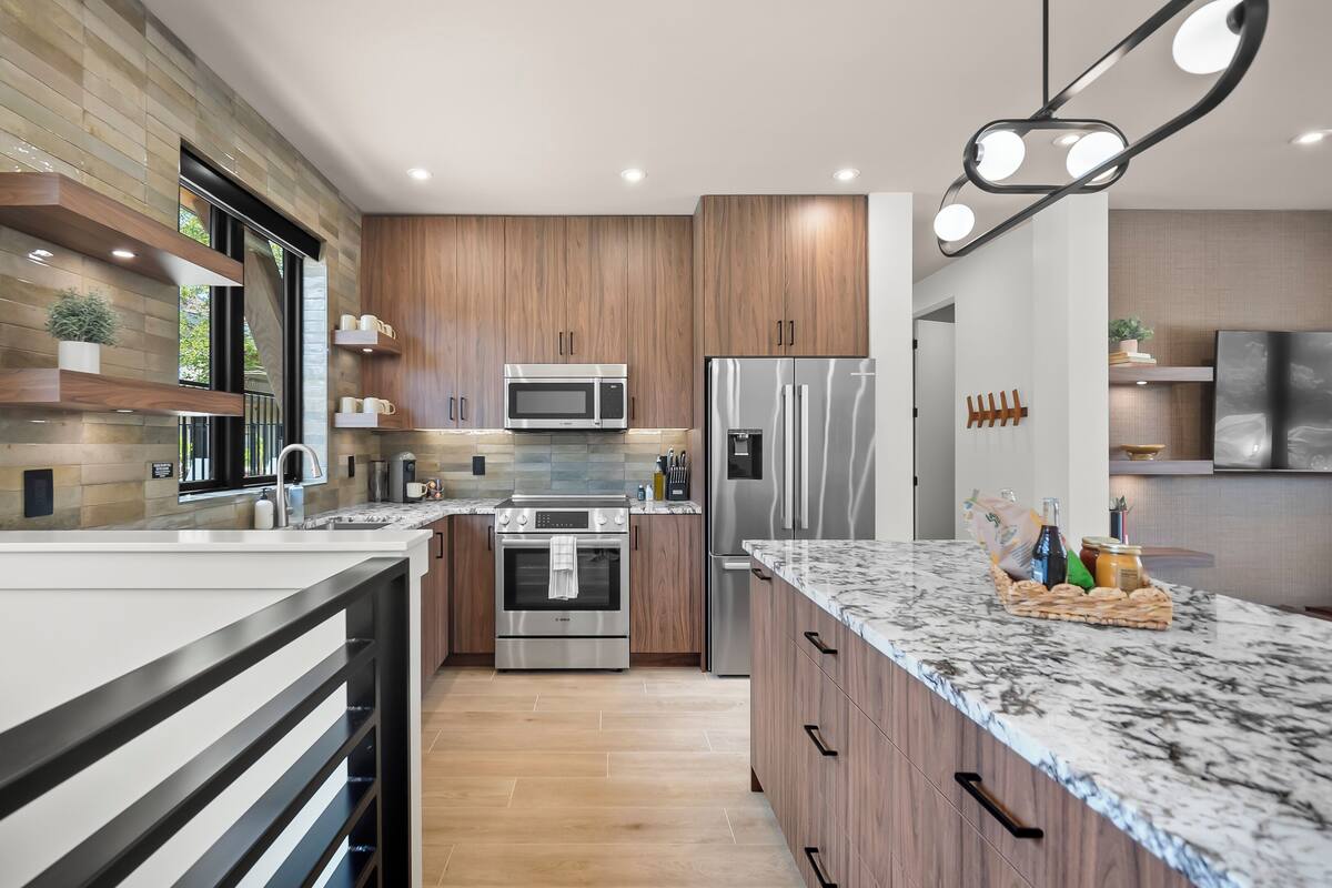 A modern kitchen with a marble countertop, stainless steel appliances, wooden cabinets, and a built-in oven.