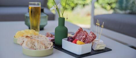 A table with a variety of food items including bread, cheese, and cured meats, accompanied by a glass of beer and a vase with flowers.