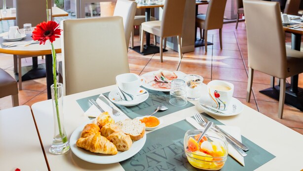A dining area with tables set for breakfast, including croissants, fruit, and coffee. - Brit Hotel Nîmes Ouest (Nîmes)