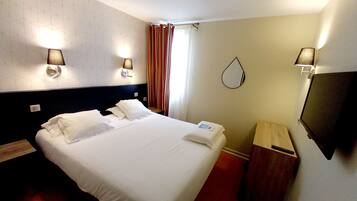 A hotel room with a bed, bedside lamps, a mirror, a TV, and a wooden nightstand.