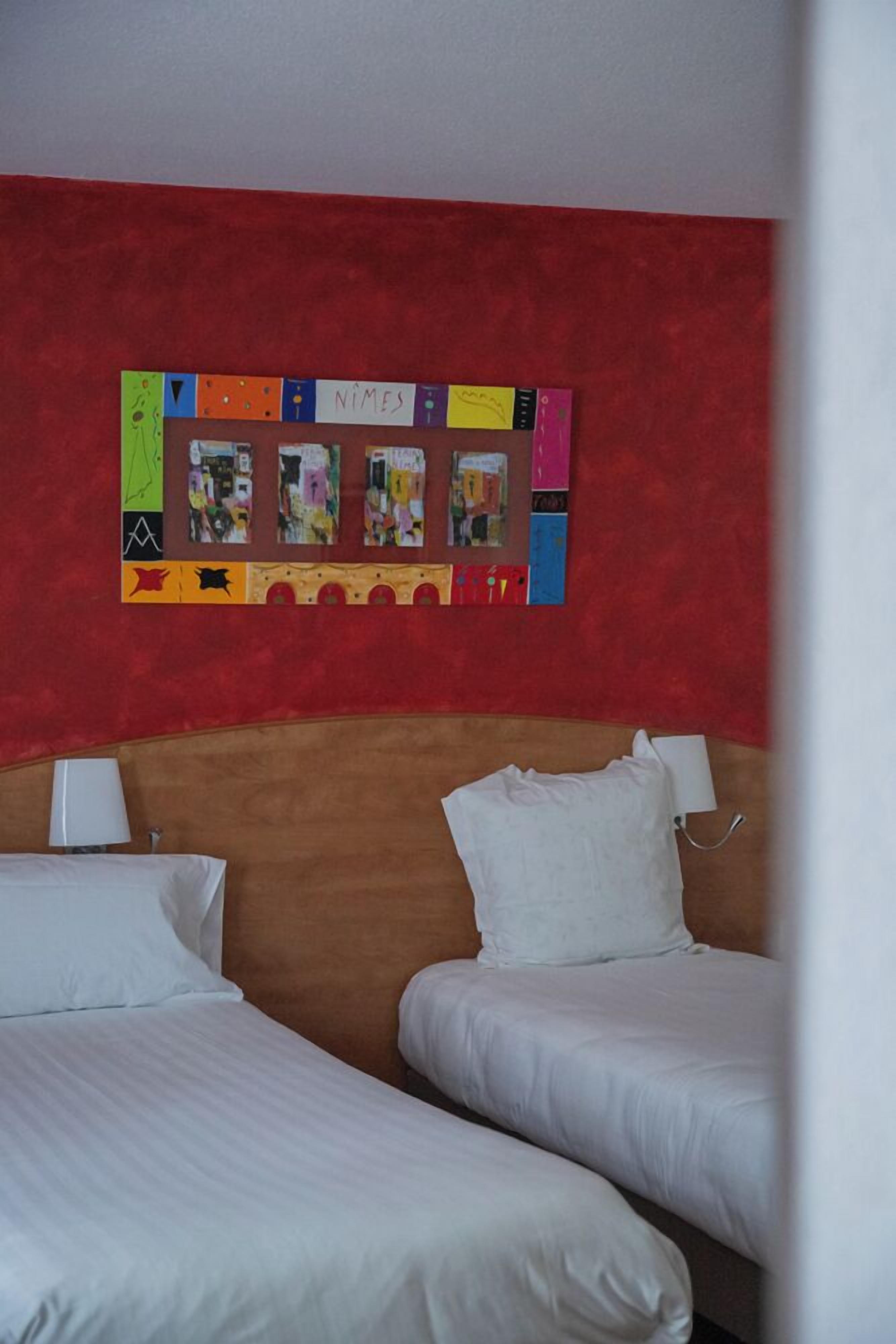 A hotel room with two beds, a red wall, and a bulletin board with various items pinned to it.