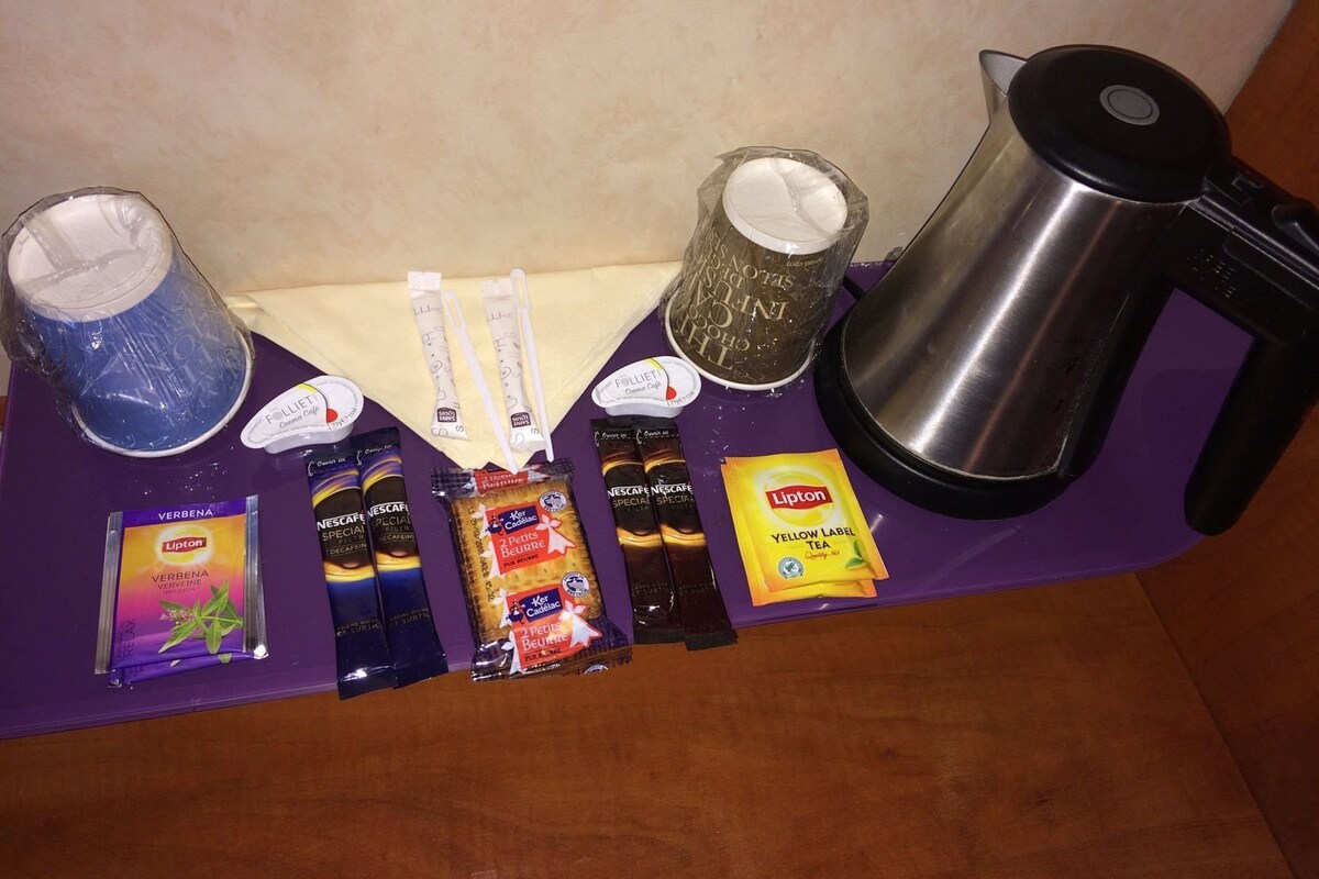 Una mesa con varios artículos, como una cafetera, un termo, bolsitas de té y aperitivos.