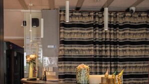 A reception area with a curved reception desk, a patterned curtain backdrop, and a vase with flowers on the counter. - Brit Hotel Nîmes Ouest (Nîmes)