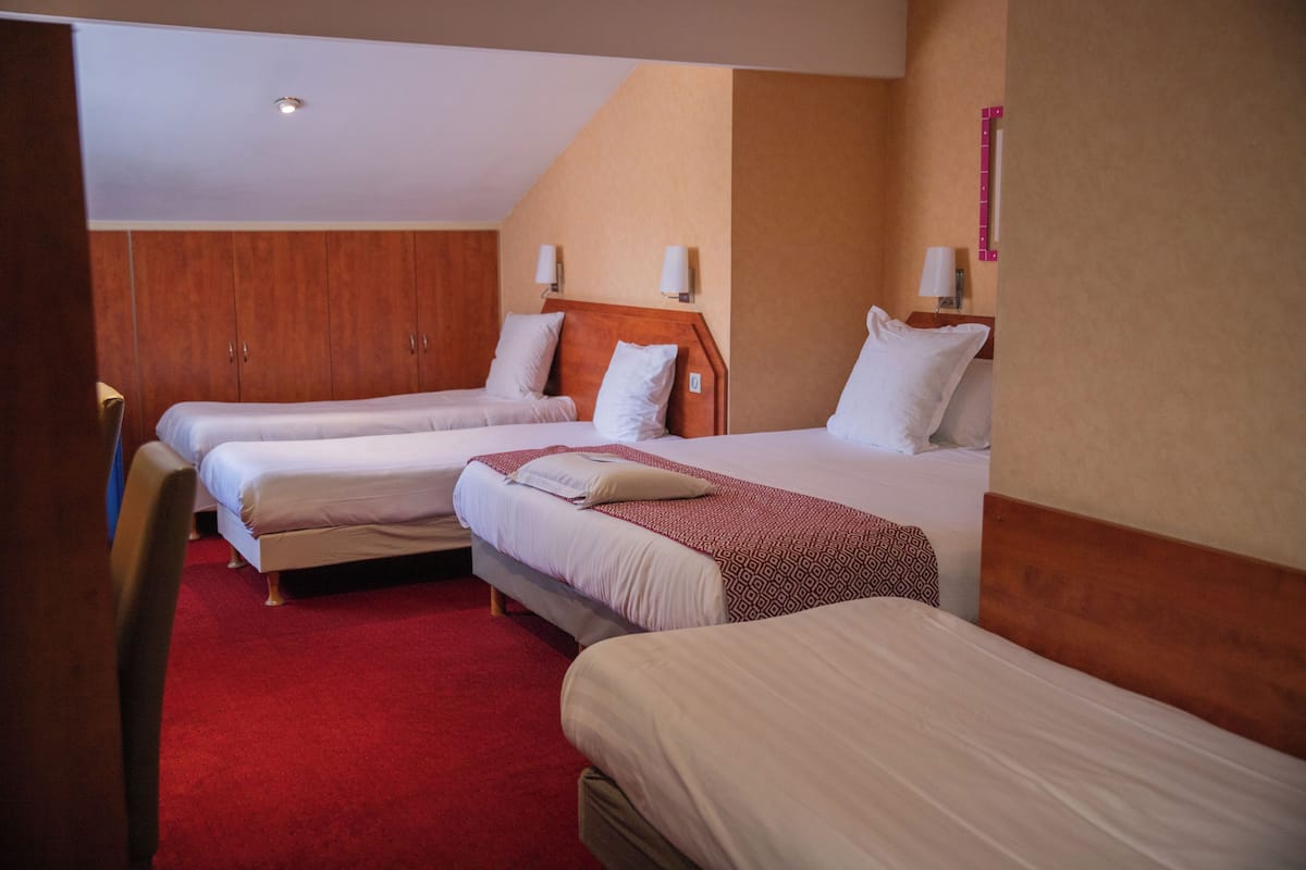 Habitación de hotel con tres camas, un armario de madera y una alfombra roja.
