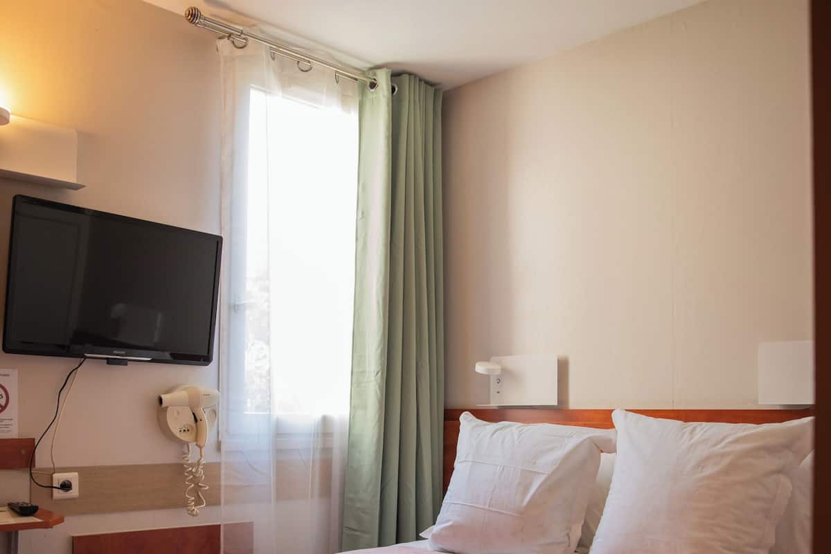 Habitación de hotel con cama, televisión montada en la pared, teléfono y ventana con cortinas.