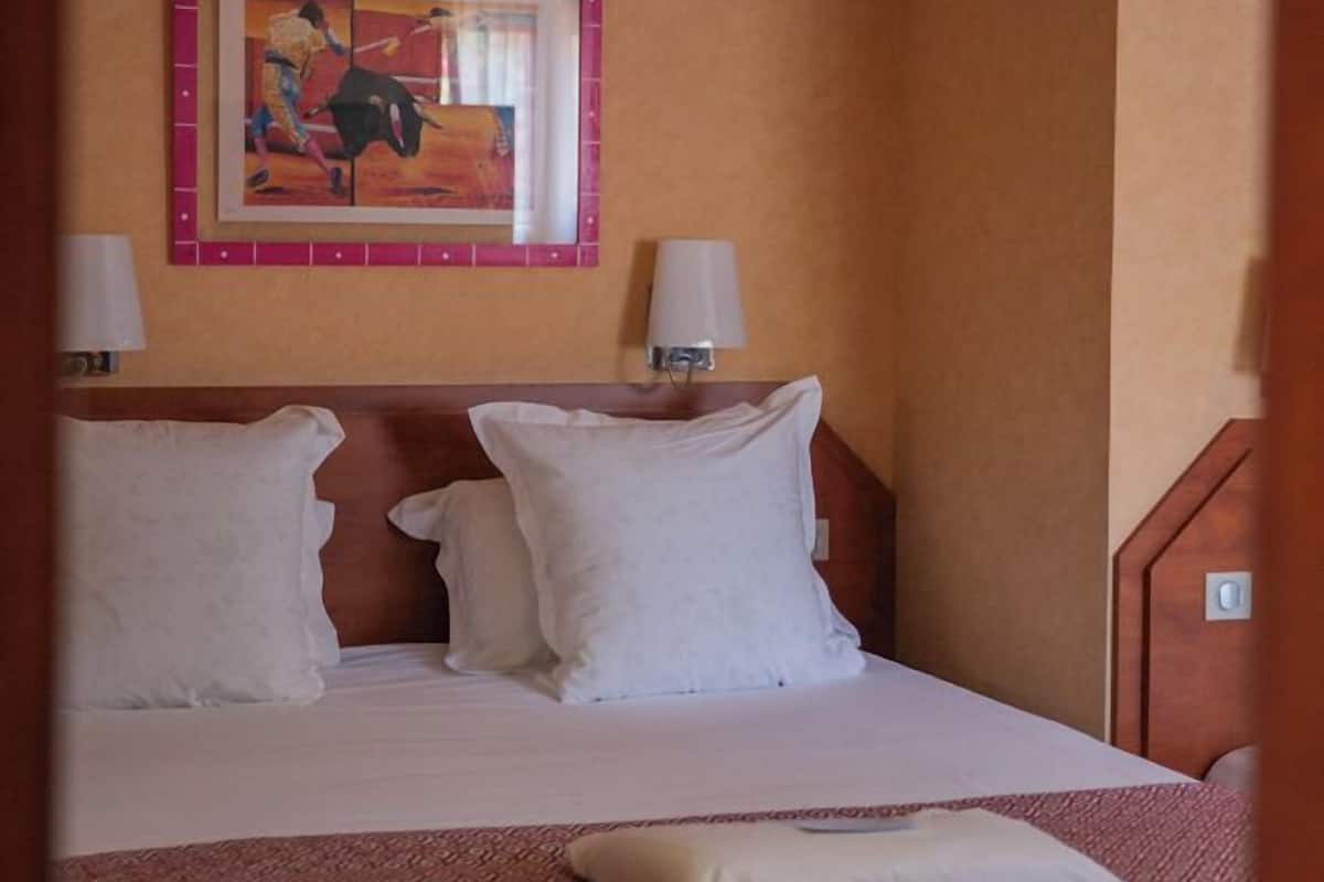 Una habitación de hotel con una cama, almohadas, un cuadro en la pared y dos lámparas de noche.