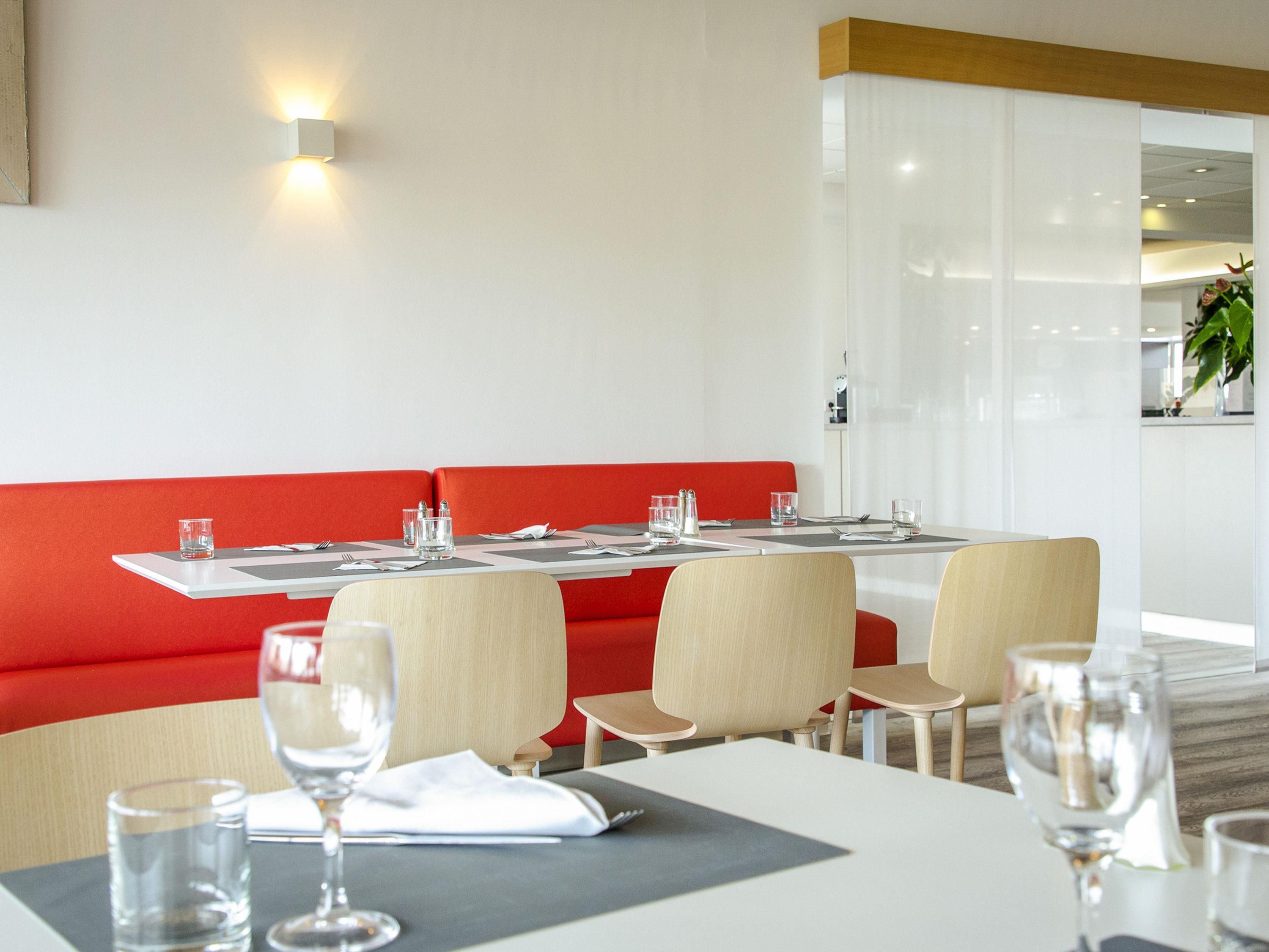 A modern dining area with a red booth seating, white tables, and a clean, minimalist design.