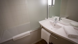 A bathroom with a bathtub, a sink, a mirror, and a towel rack. - Ibis Perpignan Nord Rivesaltes (Rivesaltes)