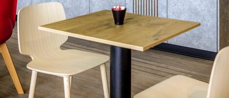 Ein kleiner Tisch mit schwarzem Gestell und Holzplatte, begleitet von zwei Stühlen mit heller Holzoptik.