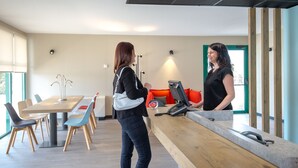 Ett välkomstområde med en receptionsdisk i trä, en sittgrupp med stolar och utsikt över utomhusmiljön genom ett fönster.