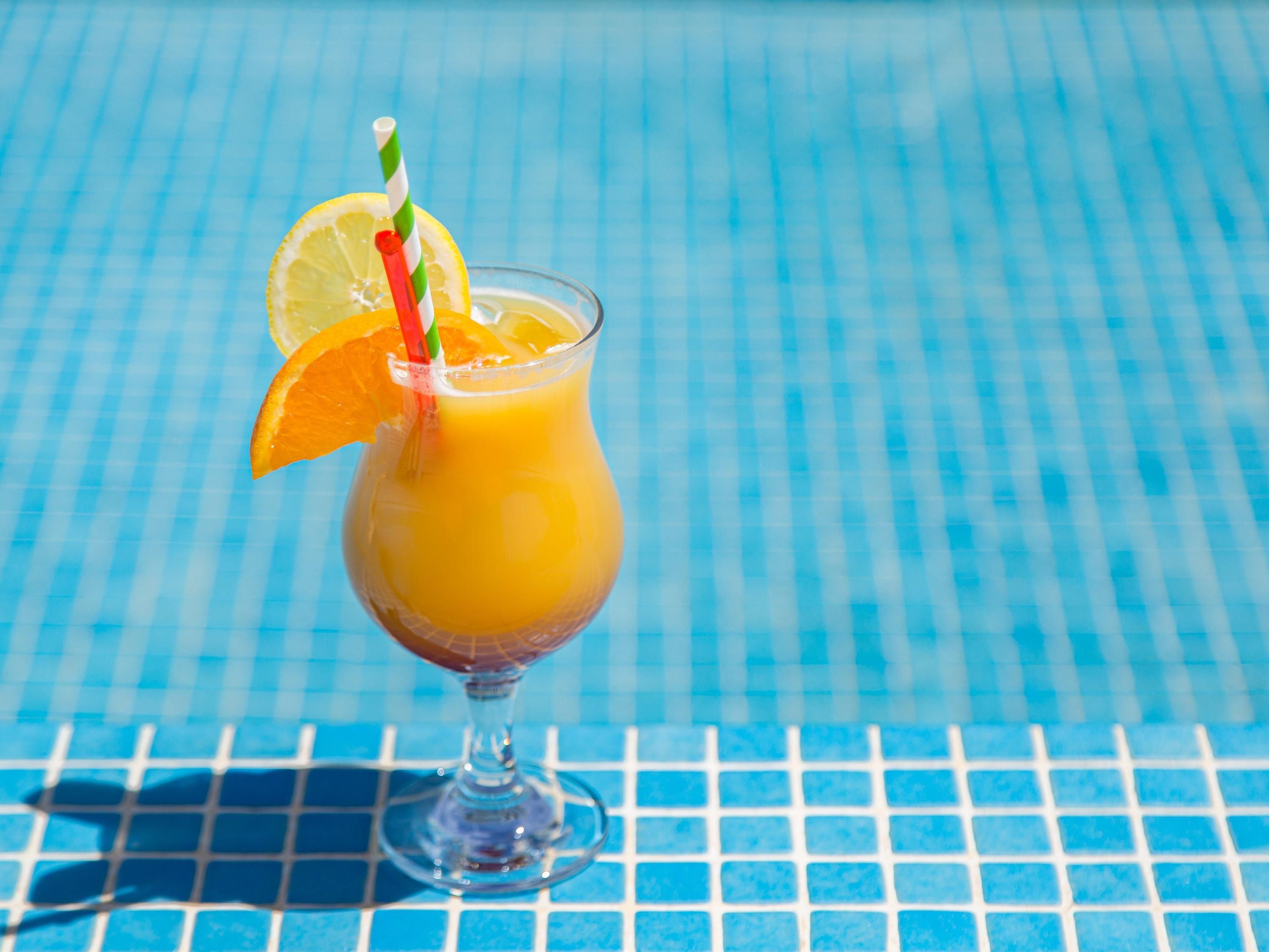 A glass of orange juice with a lemon slice and a striped straw on a blue tiled surface.