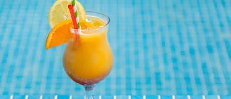 A glass of orange juice with a lemon slice and a striped straw on a blue tiled surface.