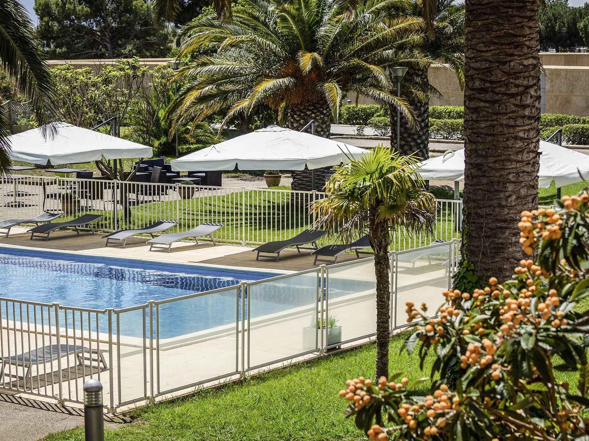 A pool area with lounge chairs and umbrellas, surrounded by palm trees and a fence.