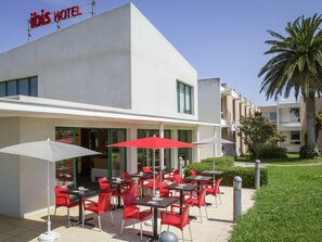 An outdoor seating area with red chairs and white umbrellas at a hotel. - Ibis Perpignan Nord Rivesaltes (Rivesaltes)
