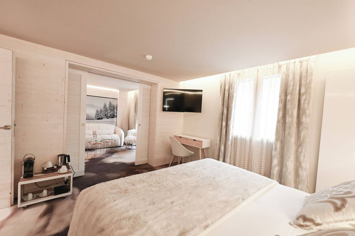 Hotelkamer met een bed, een bureau, een televisie en uitzicht op een besneeuwd landschap door een geopende deur.