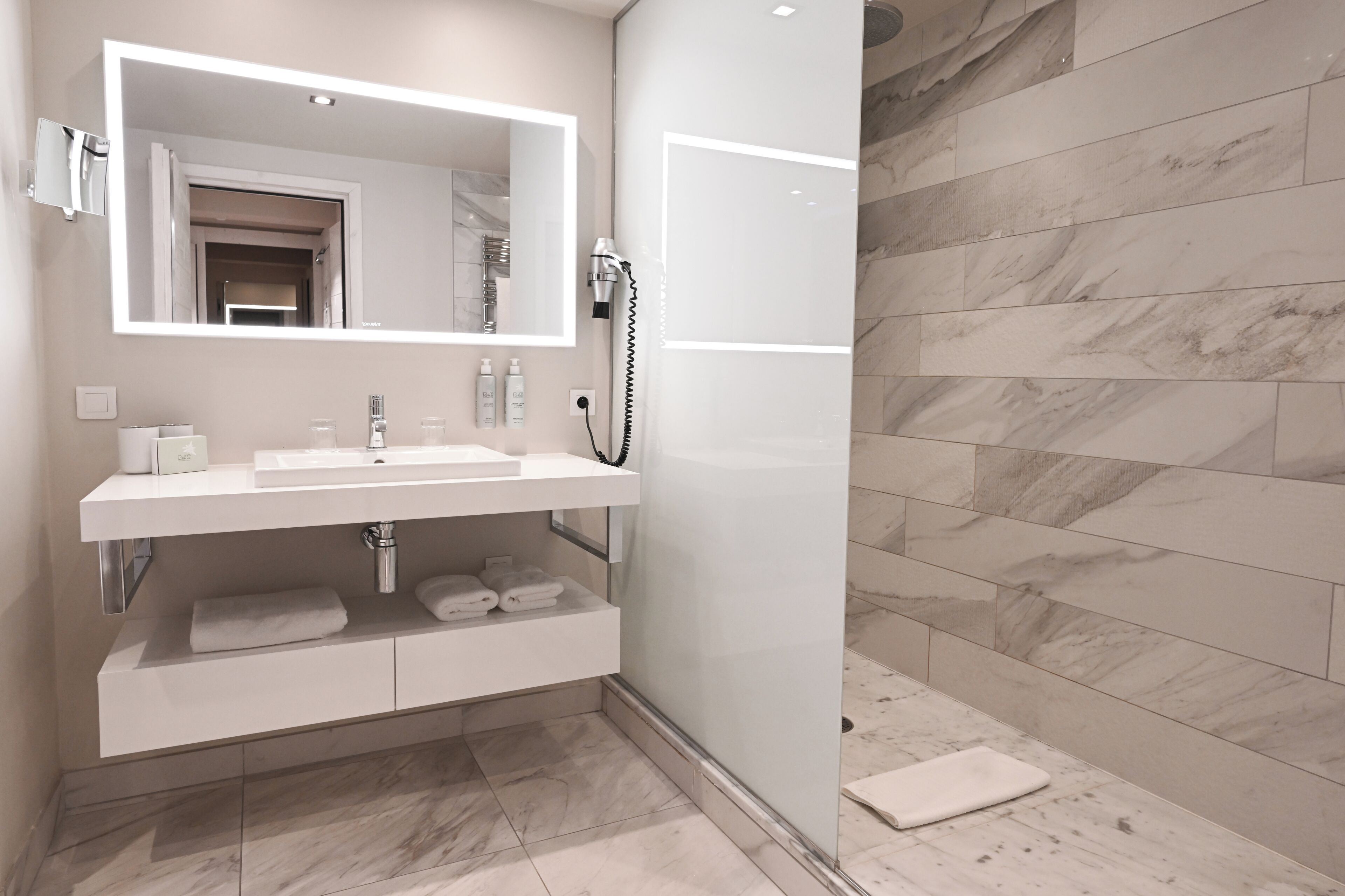 Un baño moderno con un espejo grande, tocador blanco y zona de ducha.