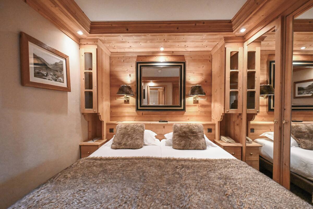 Een slaapkamer met houten lambrisering, een groot bed, twee bedlampen, een spiegel en een lijst met een afbeelding aan de muur.