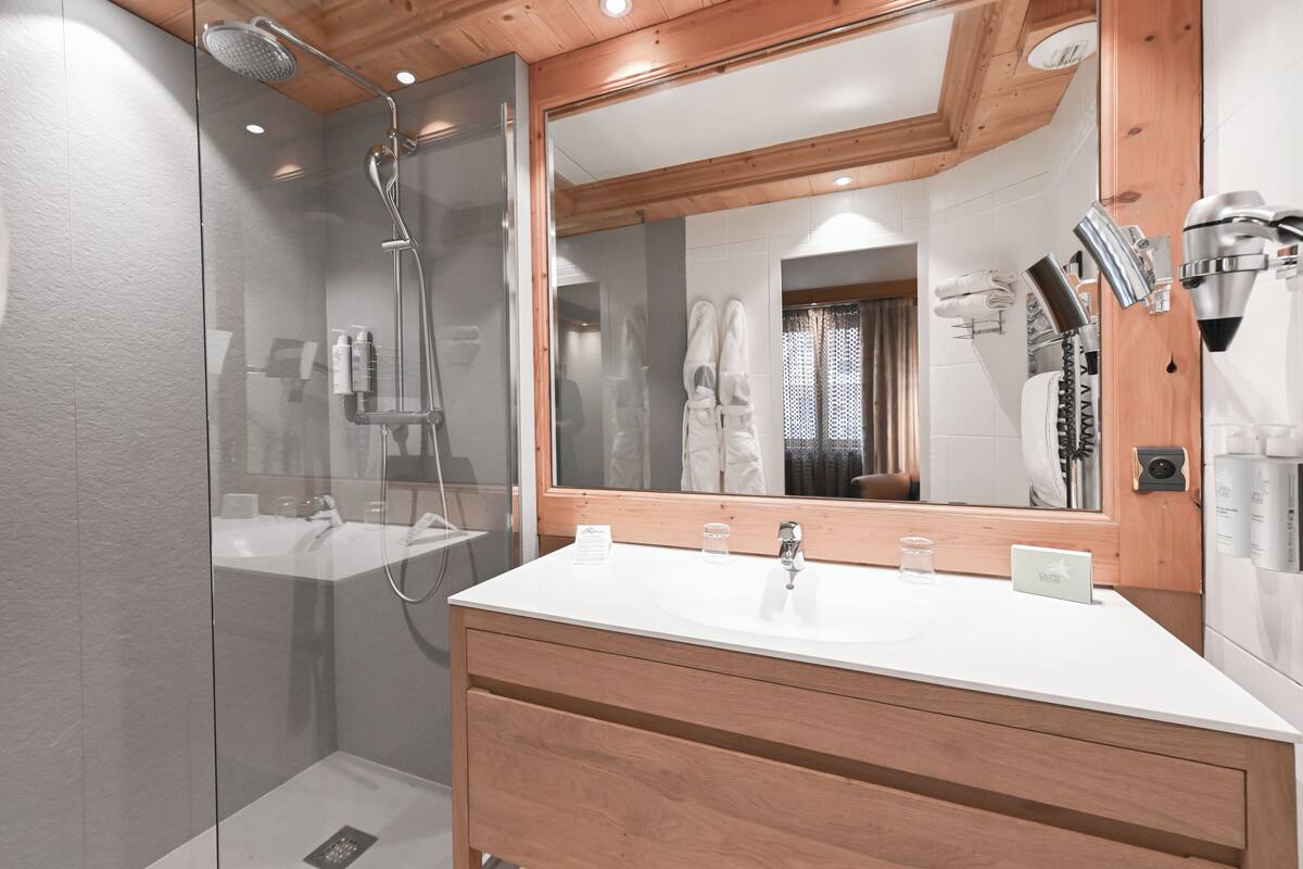 Een moderne badkamer met een douchecabine van glas, een grote spiegel en een houten wastafelmeubel.