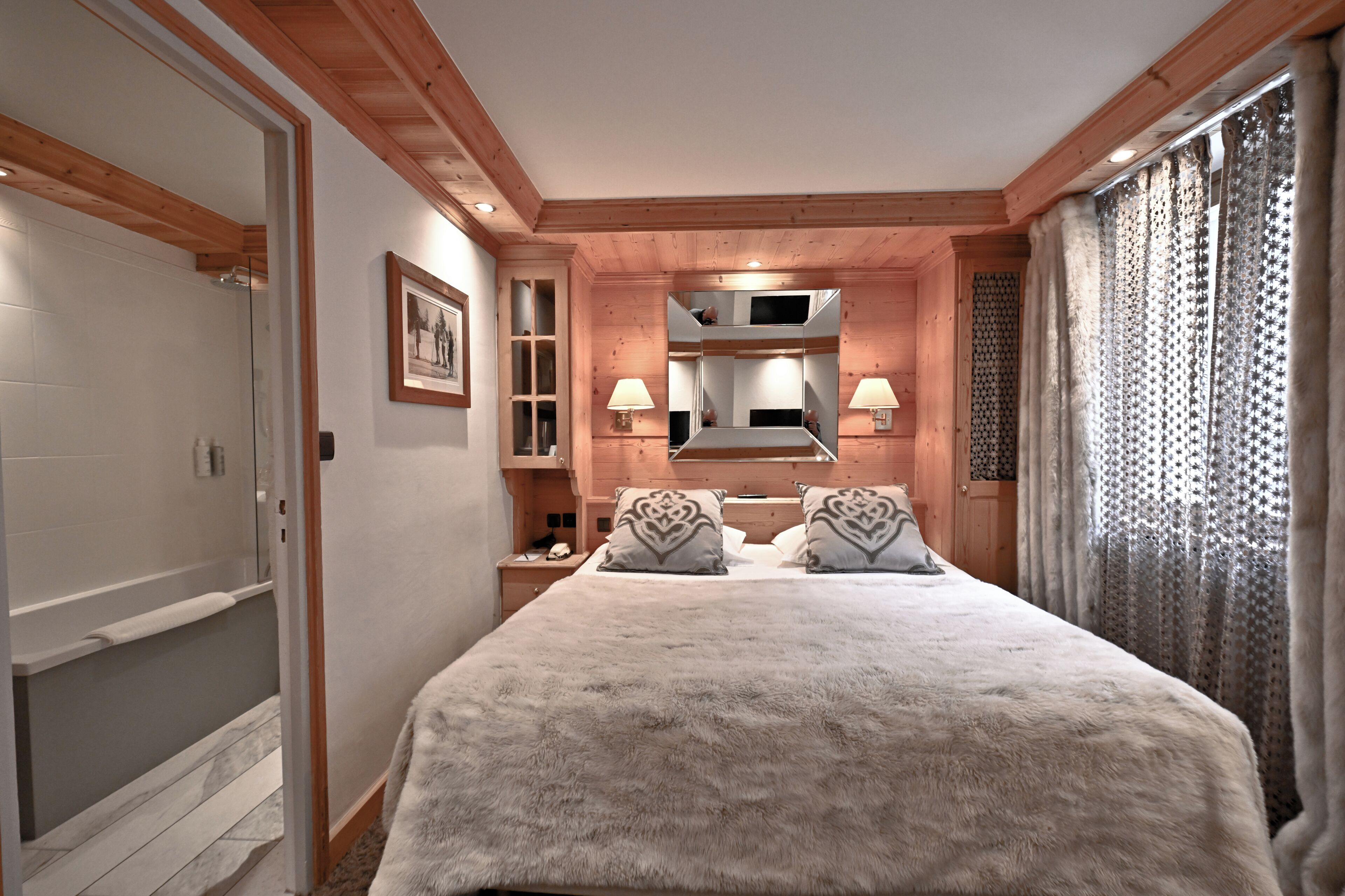A bedroom with a large bed, wooden ceiling beams, a built-in TV, and a bathroom with a shower and toilet.