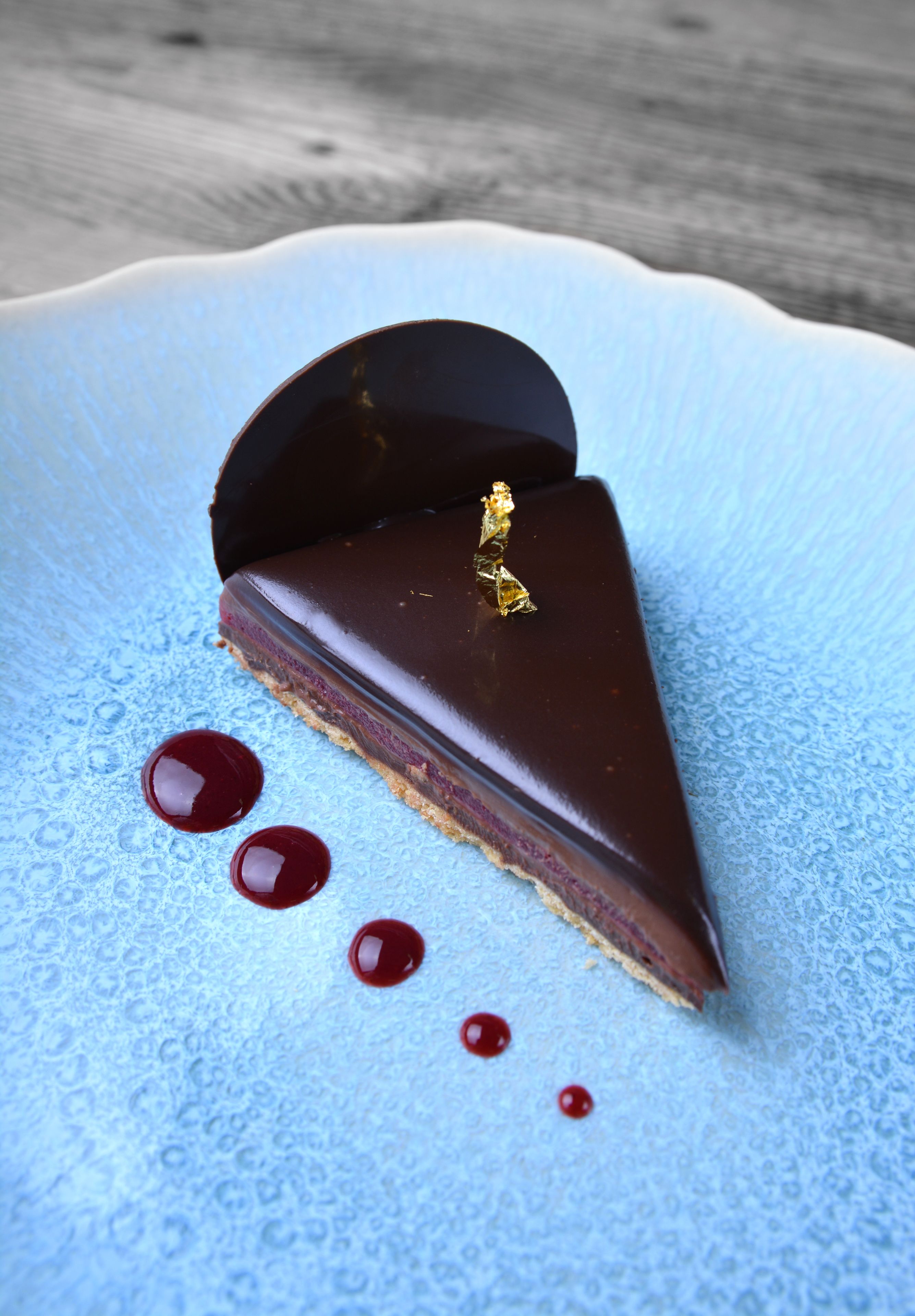 A slice of chocolate tart with a golden decoration on a blue plate with red dots.