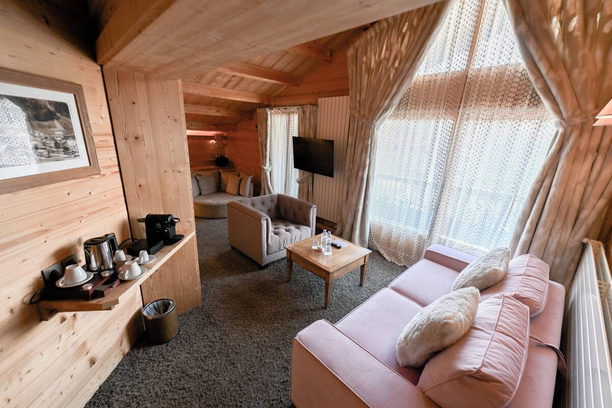 Een gezellig interieur van een chalet met een bank, fauteuil en een salontafel. Een flatscreen televisie is aan de muur bevestigd, en er hangt een lijst met een afbeelding.