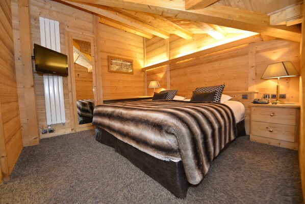 Un dormitorio de cabaña de madera con una cama, mesitas de noche, un televisor y un radiador.