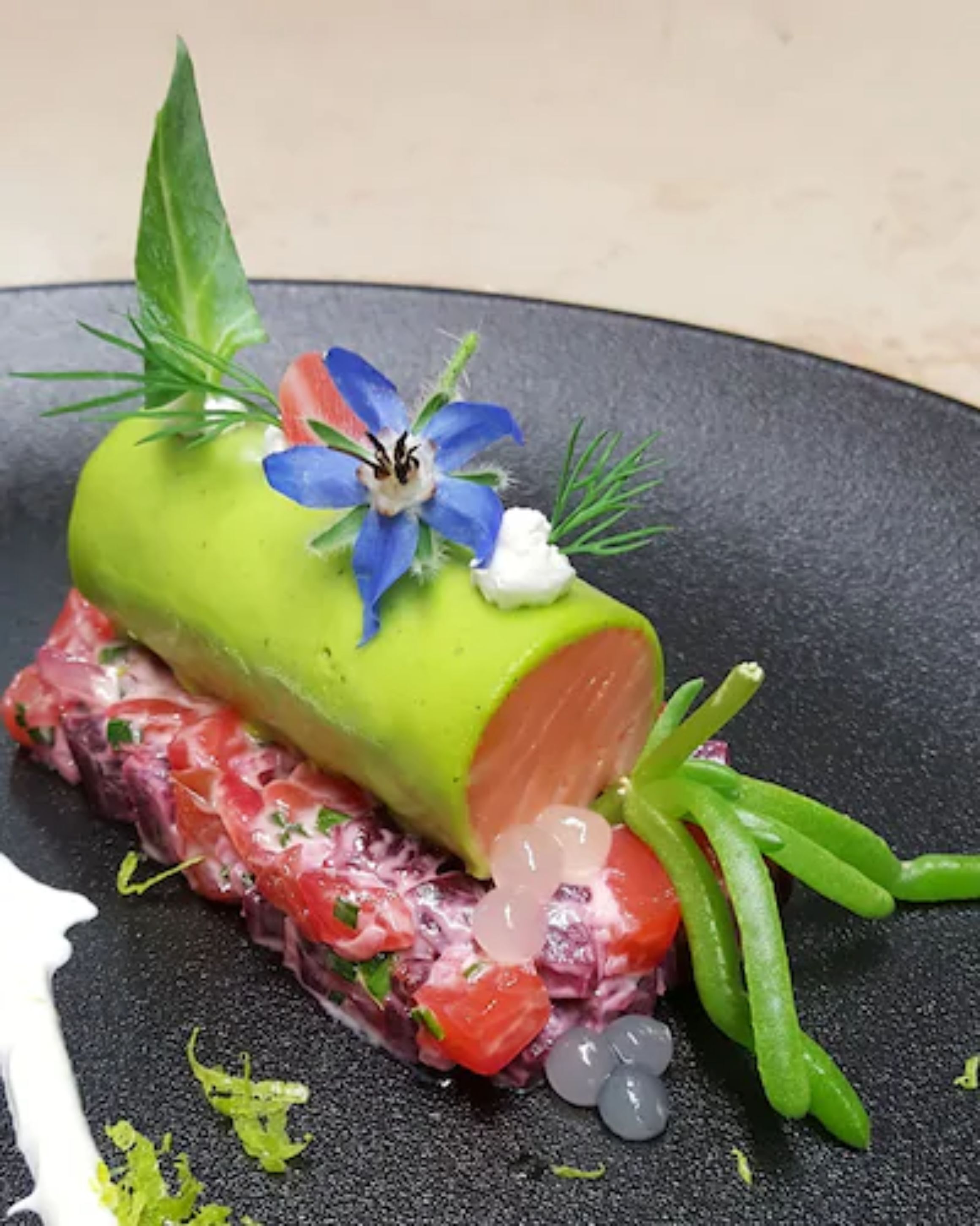 A dish with a green center, red meat, and garnishes on a black plate.