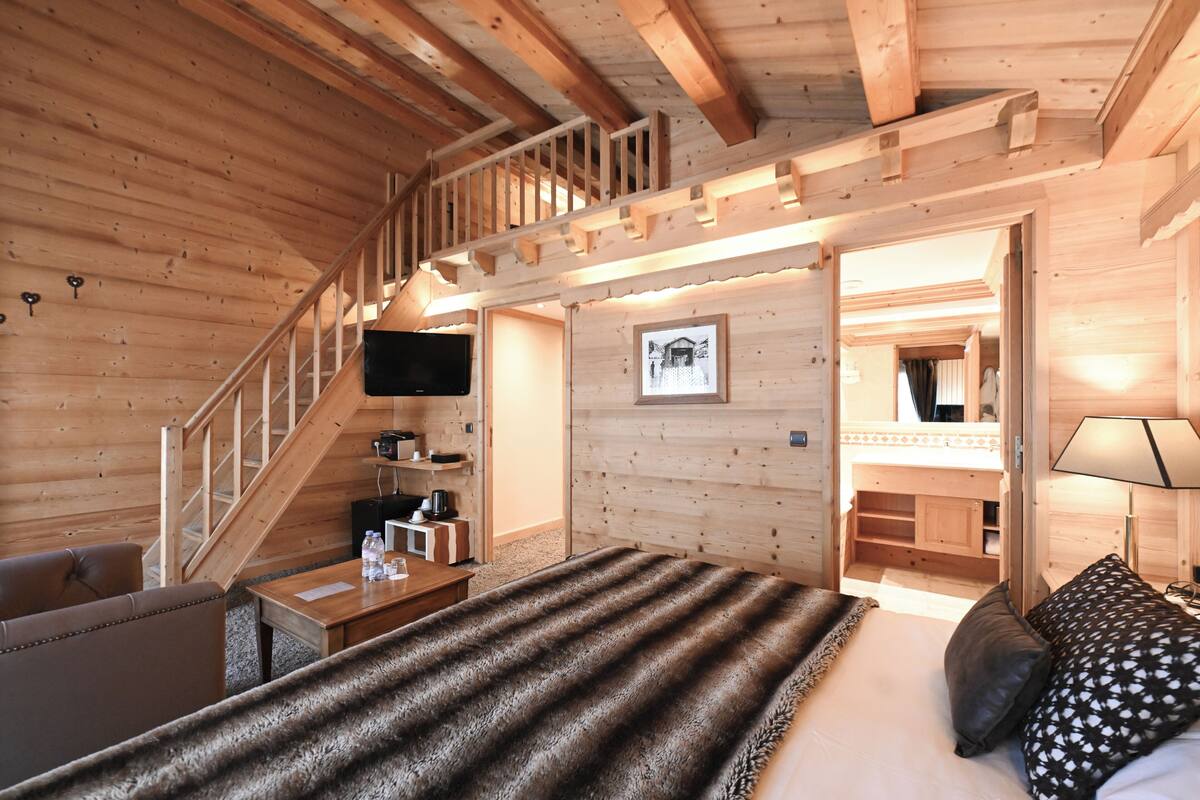 Een houten chalet met een bed, een bank, een televisie en een trap naar een hoger niveau.