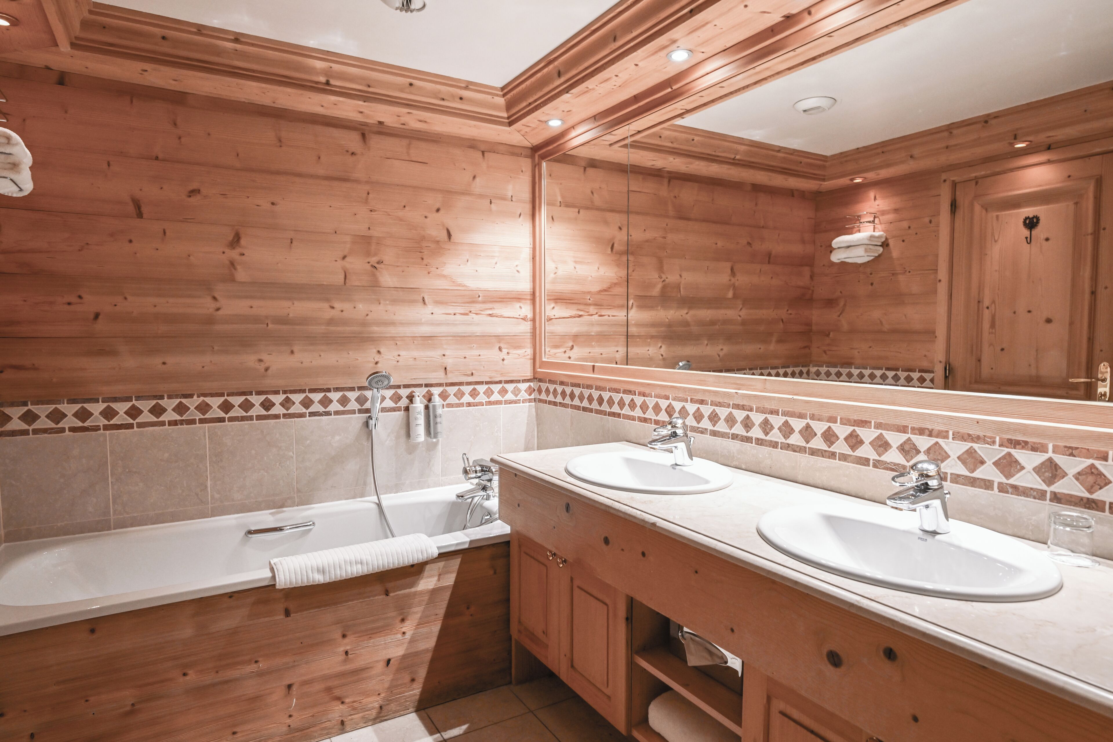 A wooden-paneled bathroom with two sinks, a bathtub, and a large mirror.