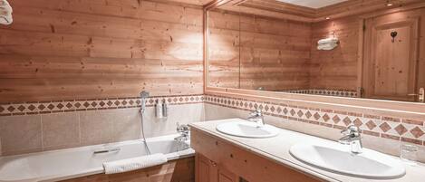 A wooden-paneled bathroom with two sinks, a bathtub, and a large mirror.