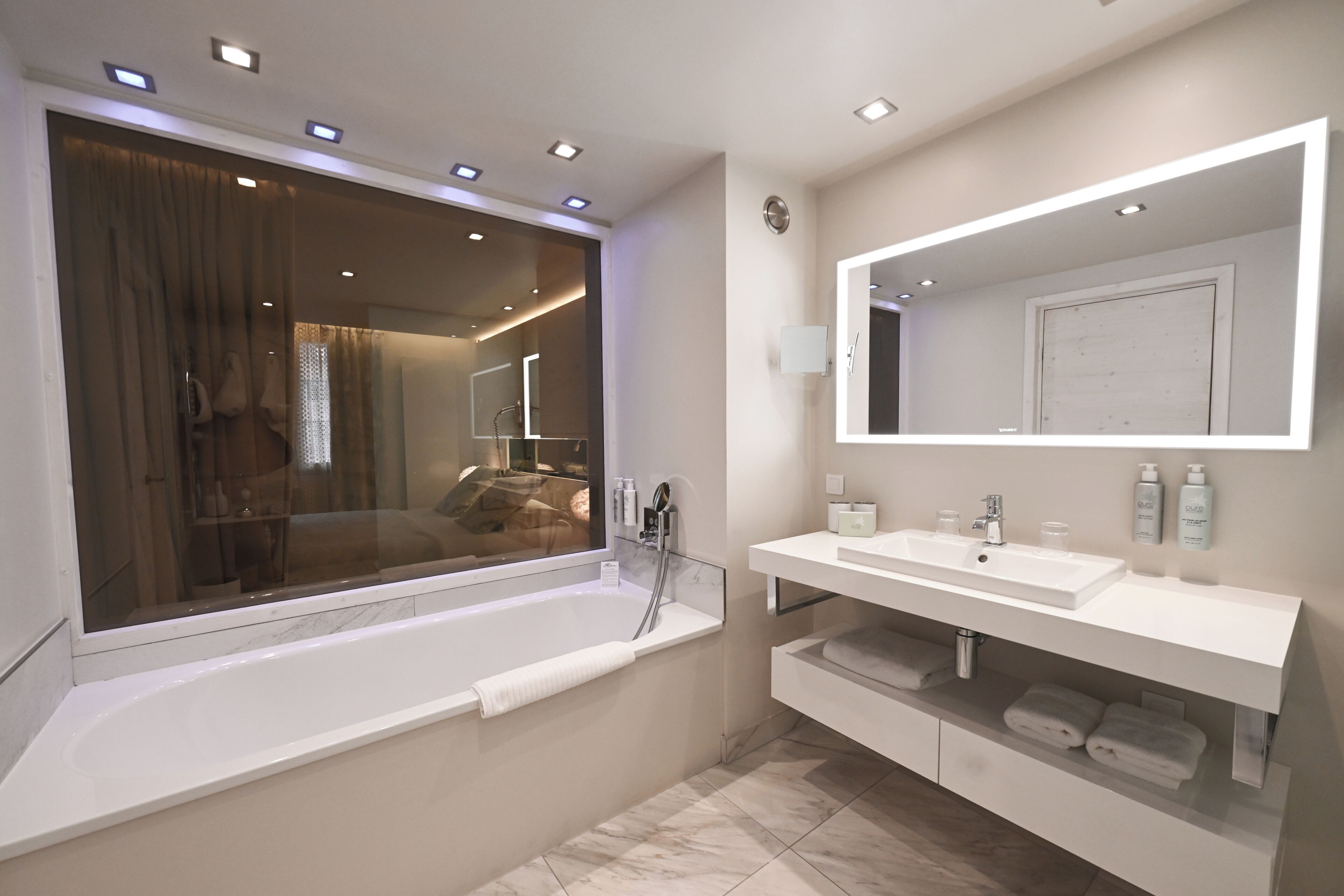 A modern bathroom with a large bathtub, a vanity with a mirror, and a window with curtains.