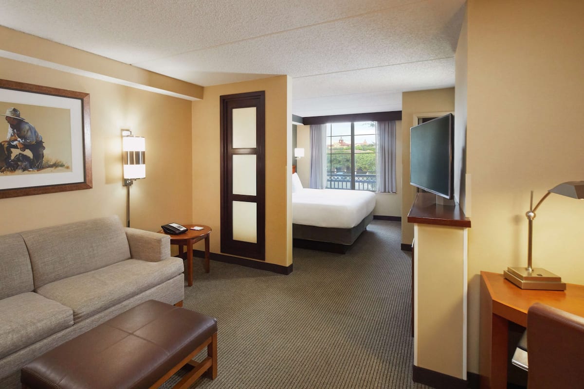 Una habitación de hotel con un sofá, una mesita, un escritorio con lámpara, una cama y un televisor.