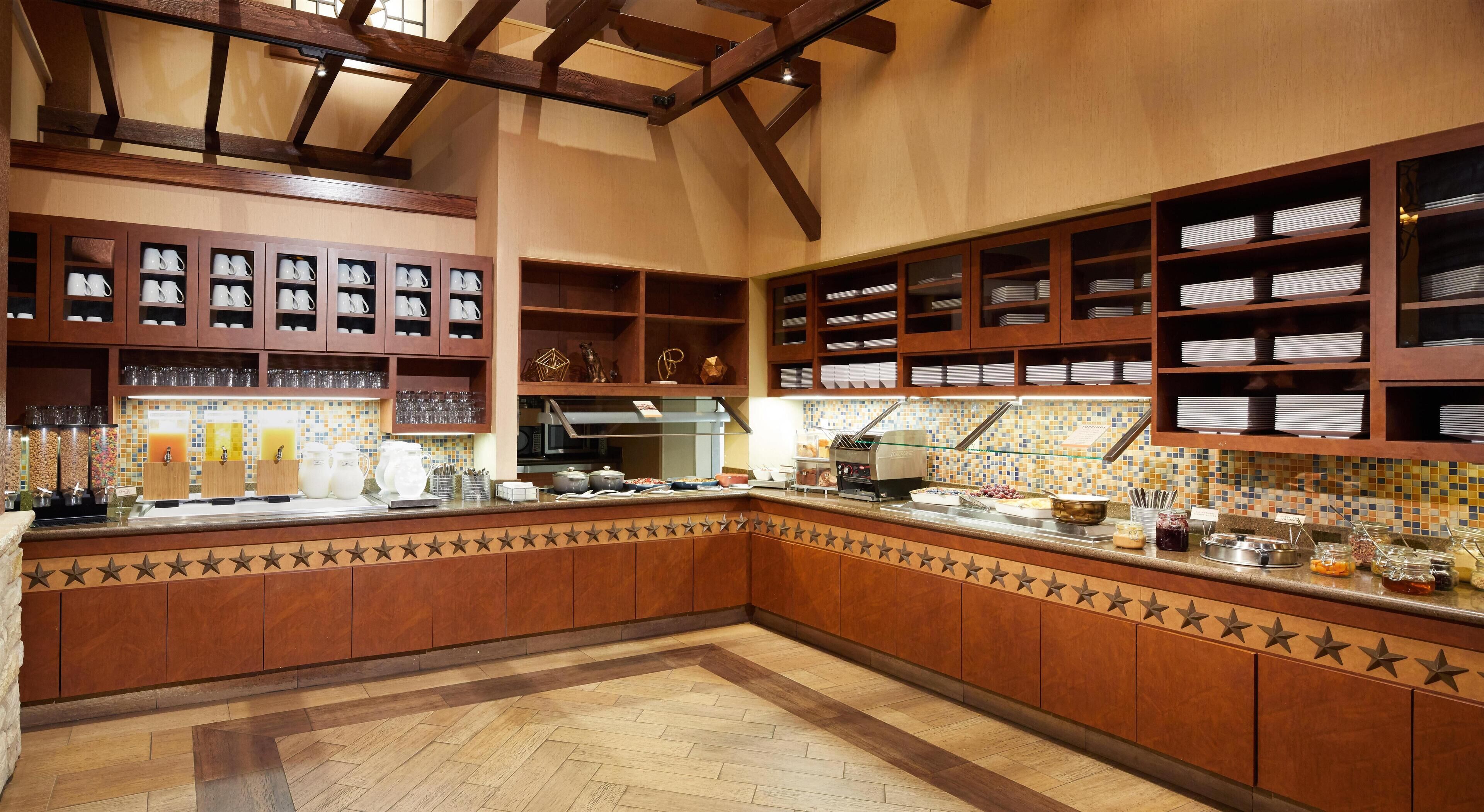 A kitchen with wooden cabinets, a tiled backsplash, and a buffet area with various food items.