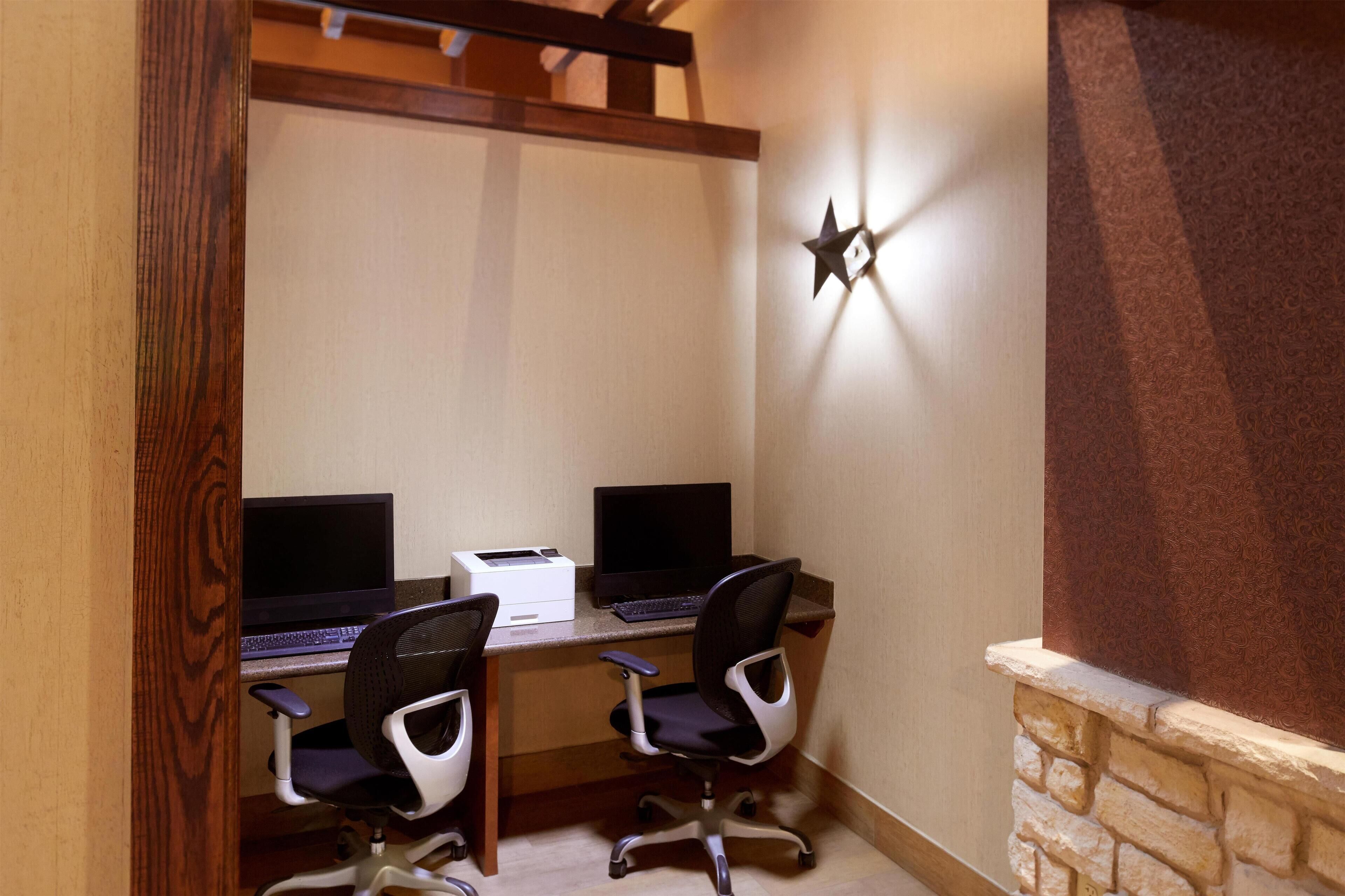 A workspace with two desks, each with a computer and a printer, and two office chairs.