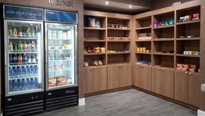 A corner market with two refrigerated beverage dispensers and wooden shelving stocked with snacks and beverages. - Fairfield Inn and Suites by Marriott Denton (Denton)