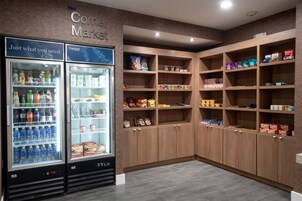 Un mercado de barrio con dos dispensadores refrigerados para bebidas y estantes de madera llenos de aperitivos y bebidas.