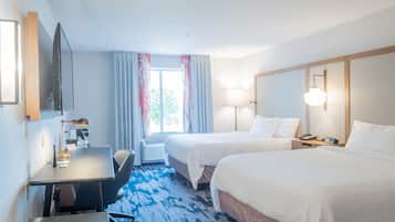 A hotel room with two beds, a desk, a chair, a TV, and a window with curtains.