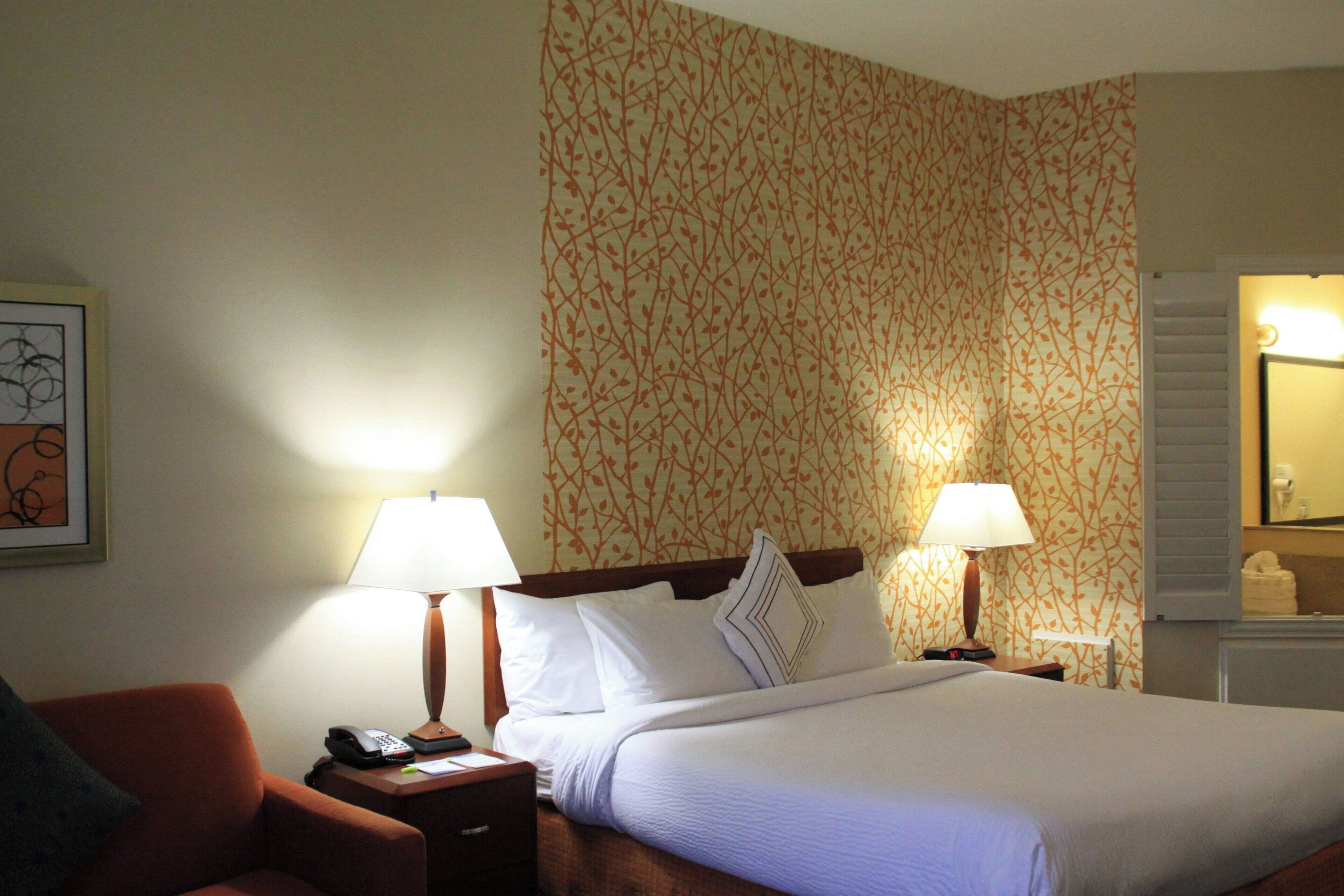 A hotel room with a bed, two bedside lamps, a nightstand with a phone, and a chair.