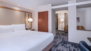 A hotel room with a large bed, a wooden wardrobe, a desk with a lamp, and a sofa. - Fairfield Inn and Suites by Marriott Denton (Denton)