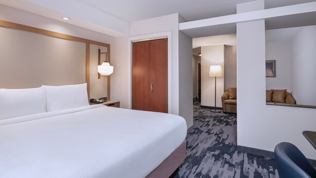 A hotel room with a large bed, a wooden wardrobe, a desk with a lamp, and a sofa. - Fairfield Inn and Suites by Marriott Denton (Denton)