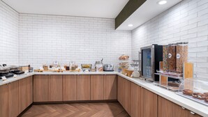 A modern kitchen with white brick walls, wooden cabinets, and a variety of food items displayed on the counter. - Fairfield Inn and Suites by Marriott Denton (Denton)