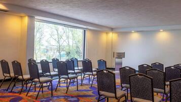 Une salle de conférence avec des rangées de chaises, une moquette à motifs, une grande fenêtre et un projecteur fixé au mur.