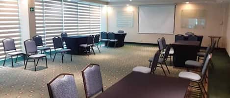 A conference room with a large table and chairs, a projector screen, and a carpeted floor.