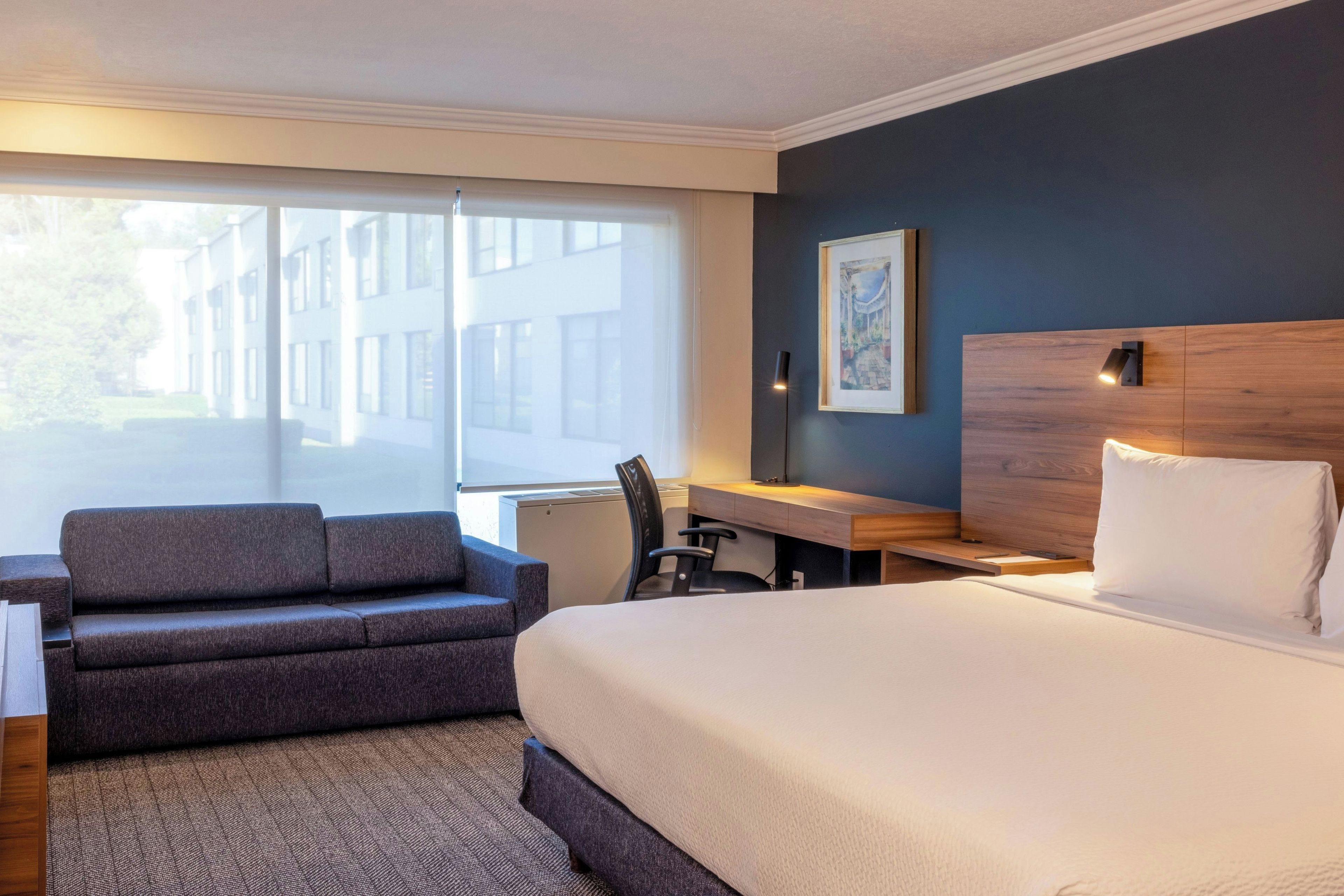 A hotel room with a large bed, a desk, a chair, and a sofa.
