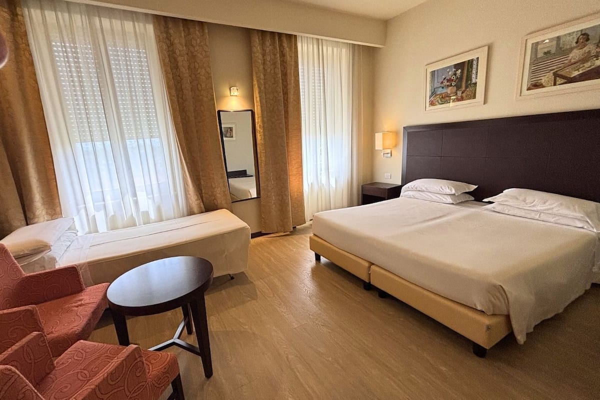 A hotel room with a bed, a desk, a chair, a mirror, and two bedside lamps.