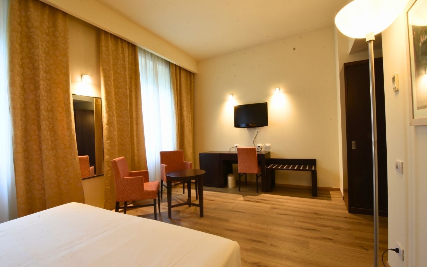 Habitación de hotel con cama, dos sillas, escritorio, televisor y una puerta.