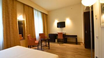 Habitación de hotel con cama, dos sillas, escritorio, televisor y una puerta.