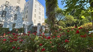A multi-story building with a gated entrance, surrounded by lush greenery and red flowers. - Hotel Terme (Montechiarugolo)