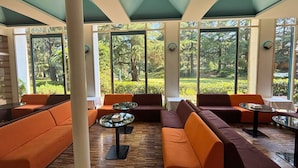 A lounge area with sofas and tables, large windows with a view of greenery, and a ceiling with geometric patterns. - Hotel Terme (Montechiarugolo)