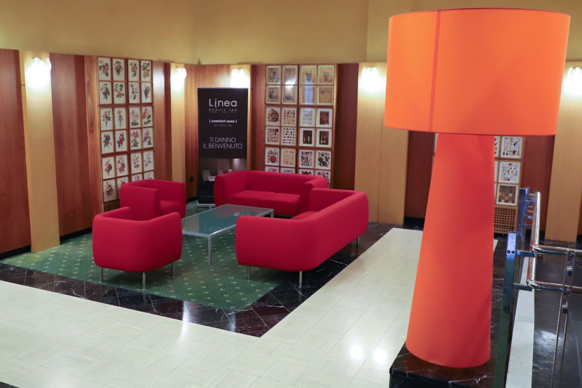A lobby with red sofas, a glass coffee table, a large orange pillar, and framed artwork on the walls.